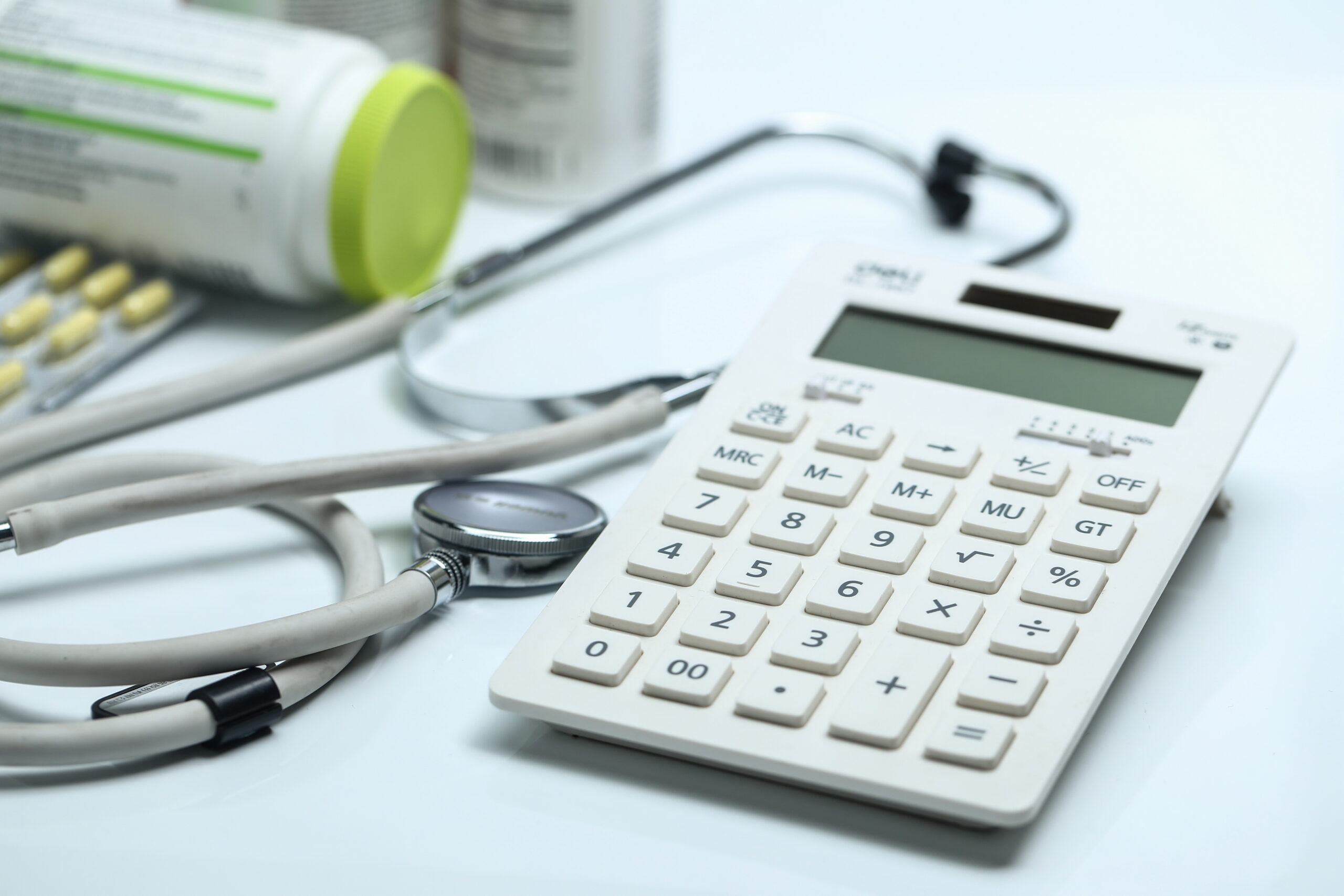 Calculadora, estetoscópio e frascos de remédio, simbolizando os custos e reajustes de plano de saúde.